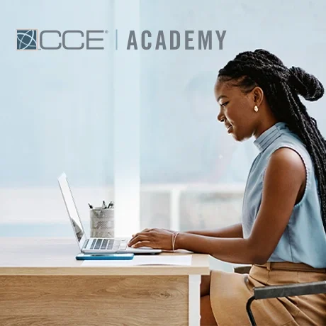 A young adult sitting at a desk working on a laptop. The CCE Academy logo is at the top.
